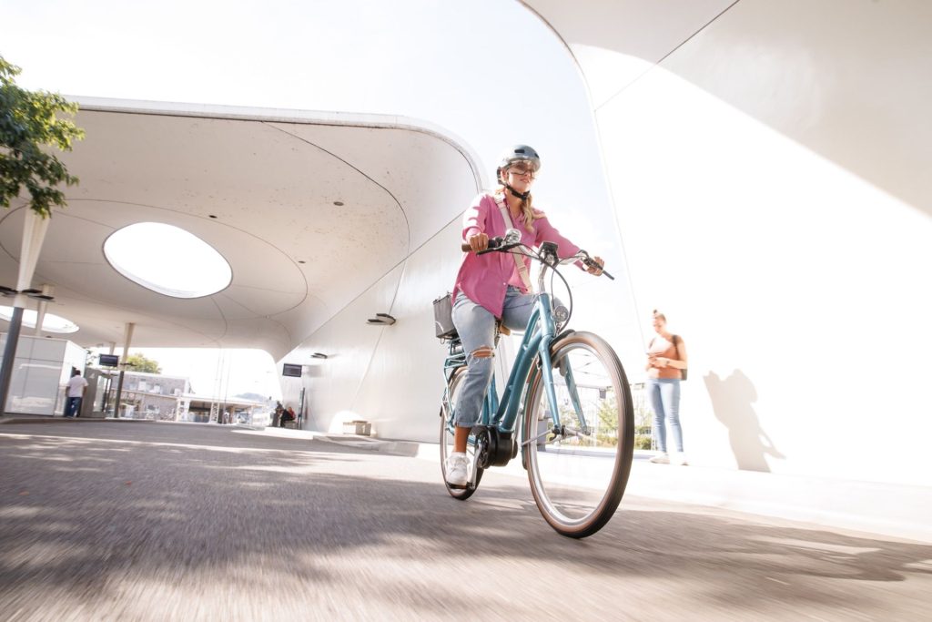 Ein Mädchen fährt in einer rosa Bluse mit dem Fahrrad durch eine moderne Stadt.